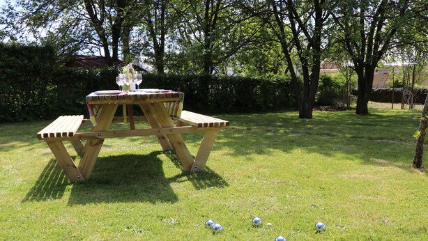 Et picnicbord med en flaske vin og glas, omgivet af en græsplæne med flere golfbolde spredt ud.