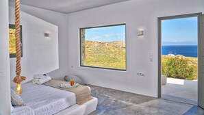 Quarto moderno com uma grande janela que oferece vista para o mar e paisagem rochosa.