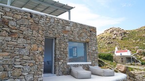 Um edifício de pedra com design moderno, destacando uma grande janela e uma área coberta para estar ao ar livre.