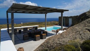 Uma área de estar coberta ao ar livre com piscina, com vista para a paisagem costeira.