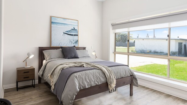 Een slaapkamer met een groot raam, een bed met hoofdeinde, een nachtkastje en een lamp.