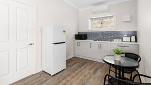 Een compacte keuken met witte kastjes, een witte koelkast, een zwarte magnetron en een klein eethoekje met een glazen tafel en stoelen.