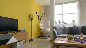 Una sala de estar con televisor, una silla colgante, un sofá y una mesa de centro con fruta y una botella.