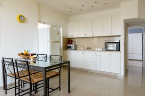 A modern kitchen with white cabinets, a glass dining table, and a microwave. - Sweet Home At Hilton Beach 2BR (Tel Aviv)