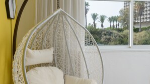 Una habitación con una silla colgante, un ventanal y vistas a palmeras y edificios.