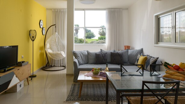 Una sala de estar moderna con un sofá, una mesa de centro de vidrio, un televisor y un sillón colgante.