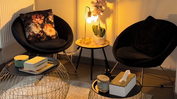 A modern living room with two black chairs, a round mirror, a small table with a lamp and flowers, and a wire coffee table with books and candles. - Hôtel du MontLouis (Paris)