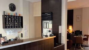 A reception area with a wooden counter, a clock, and a wall-mounted shelf with various items. - Hôtel du MontLouis (Paris)