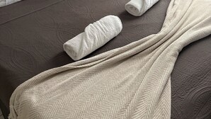 A neatly made bed with a brown bedspread, two rolled white towels, and a beige throw blanket. - Hôtel du MontLouis (Paris)