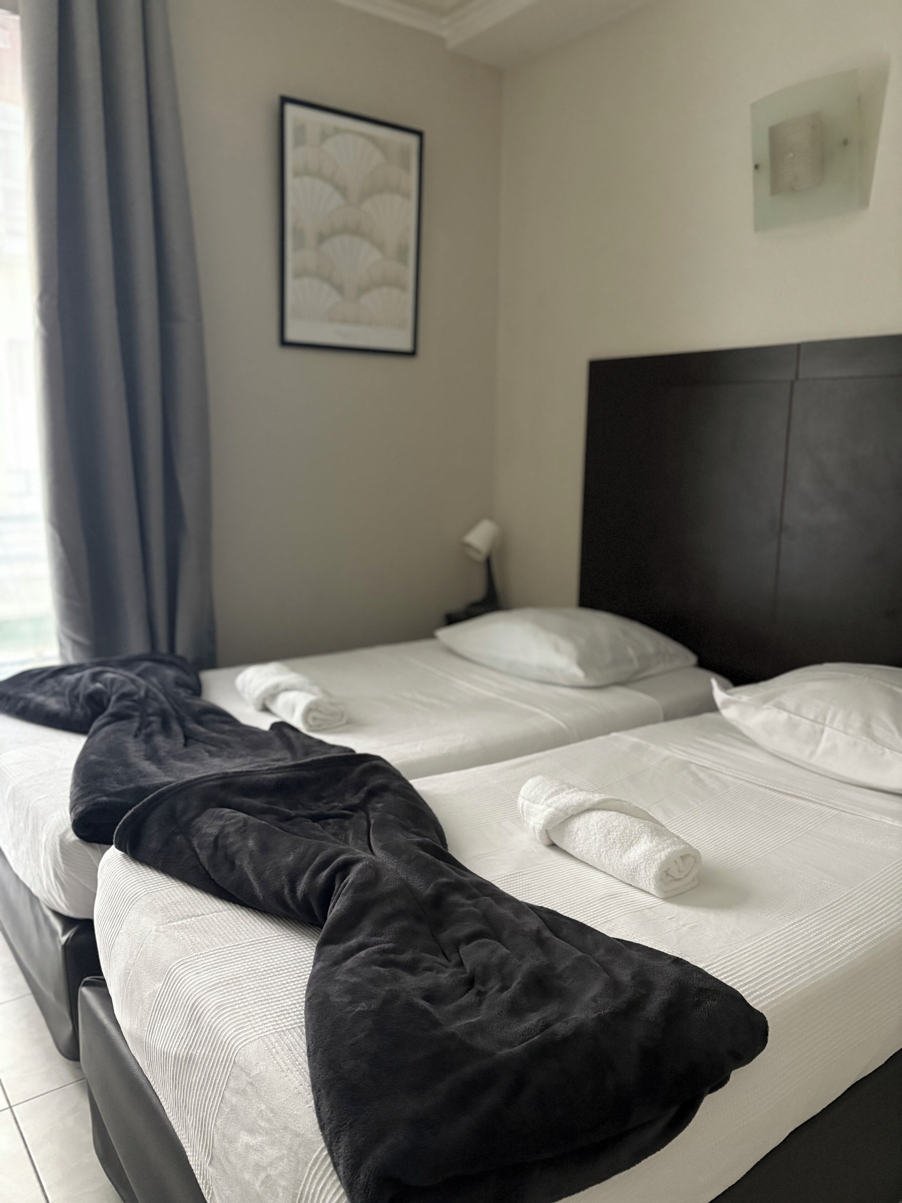 A hotel room with two beds, a dark headboard, a framed artwork on the wall, and a window with curtains.
