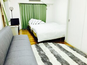 Ein kleiner, kompakter Raum mit Bett, Sofa, Fernseher und einem grünen Vorhang.