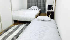 Ein kleines, sauberes Zimmer mit zwei Betten, einem Fernseher und einem Fenster mit Vorhängen.