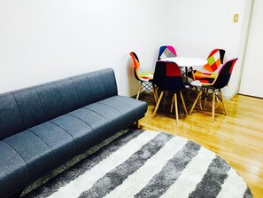 A modern living room with a grey sofa, a striped rug, and a table with colorful chairs.