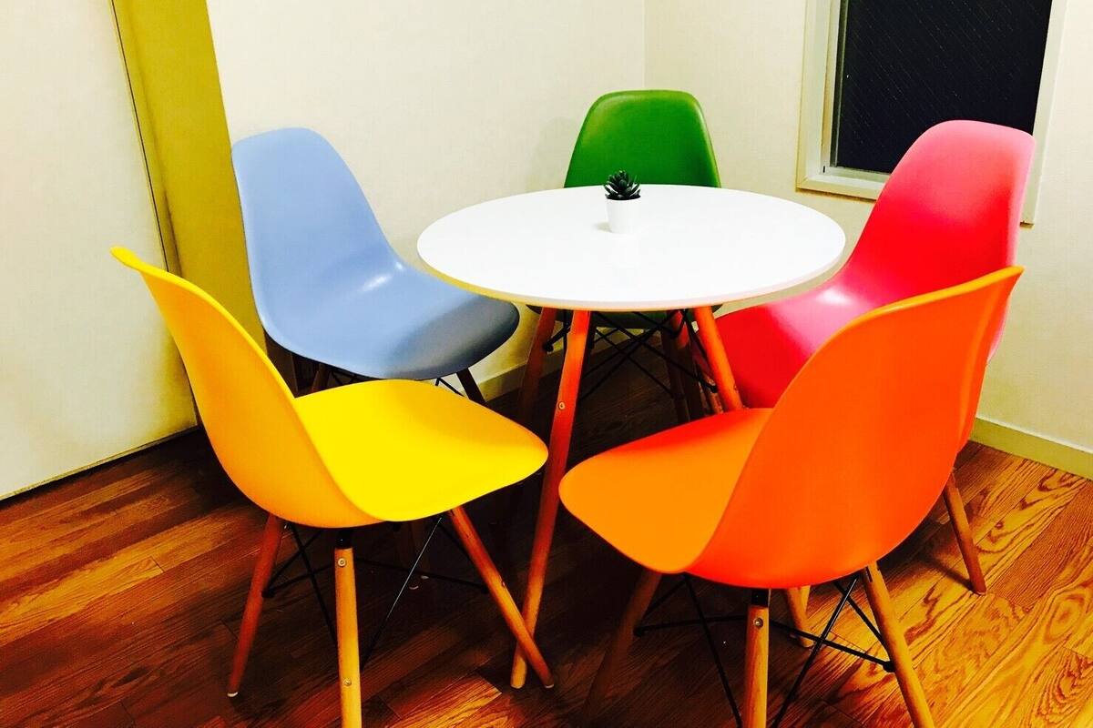 A small room with a round white table and four colorful chairs (yellow, blue, green, and red) around it.