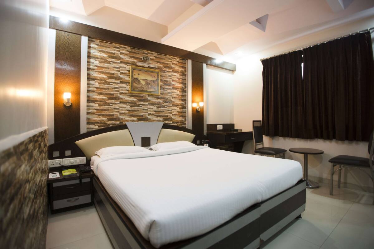 A modern hotel room with a large bed, a stone accent wall, a desk, and a small seating area.