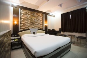A modern hotel room with a large bed, a stone accent wall, a desk, and a small seating area. - Hotel Three Star Pvt Ltd (Panvel)
