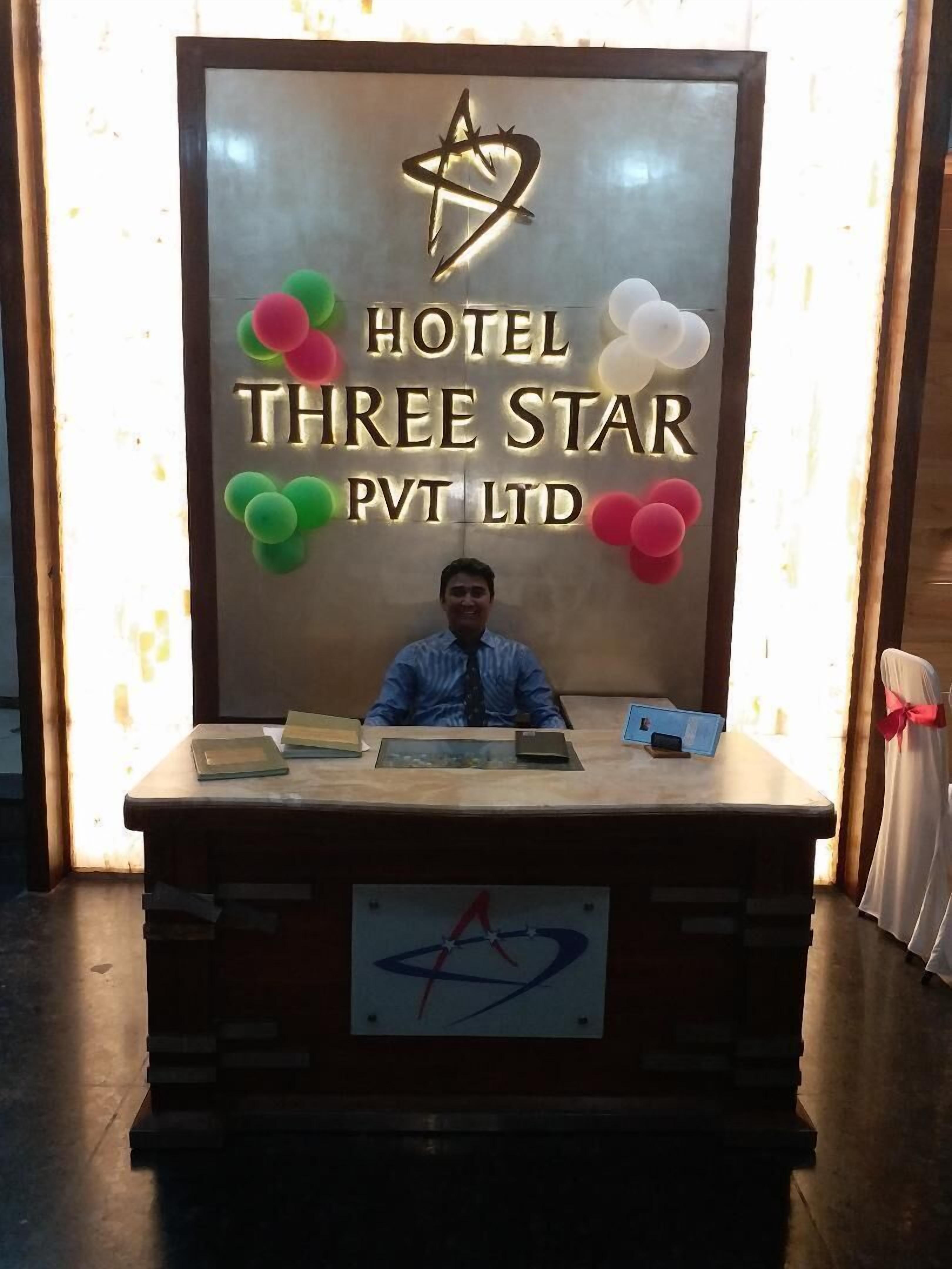 Vastaanottotiski, jossa on kyltti, jossa lukee ”Hotel Three Star Pvt Ltd”, ja sen yläpuolella hotellin logo.