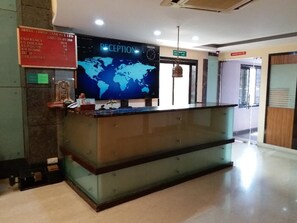 A reception desk with a world map, a clock, and a sign listing currency exchange rates. - Hotel Three Star Pvt Ltd (Panvel)