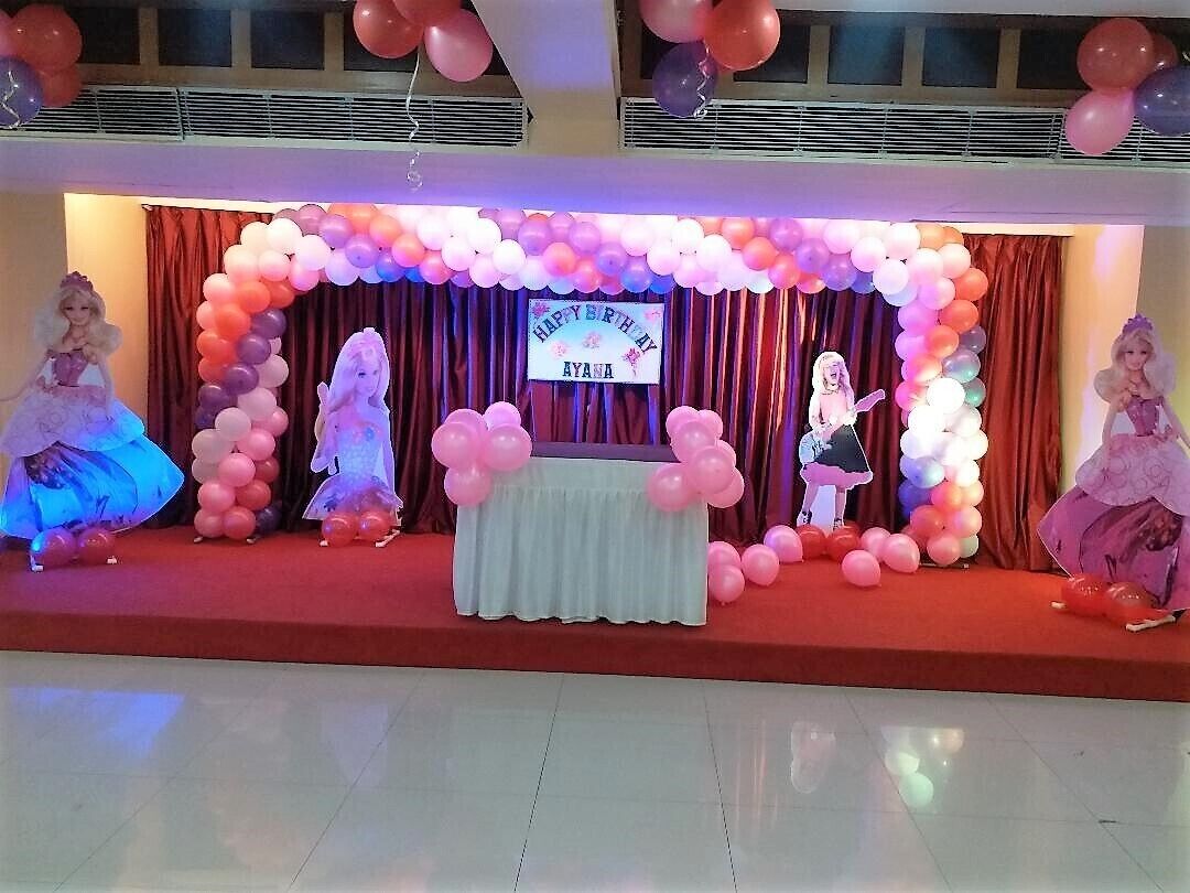 A stage with a birthday banner, balloons, and dolls.
