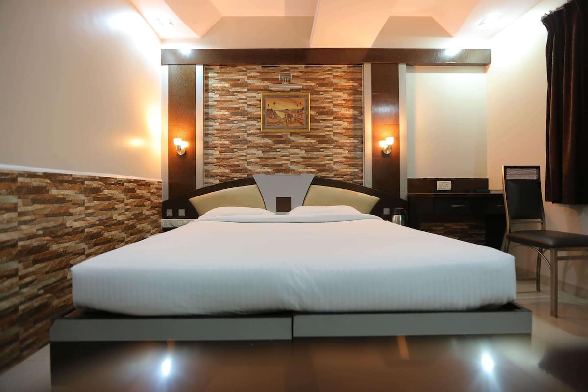 A modern hotel room with a large bed, a stone accent wall, and a desk with a chair.