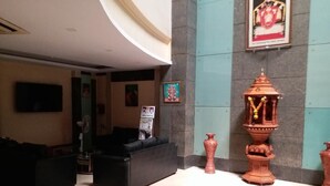 A lobby with a black sofa, a television mounted on the wall, a framed picture, and a decorative urn. - Hotel Three Star Pvt Ltd (Panvel)