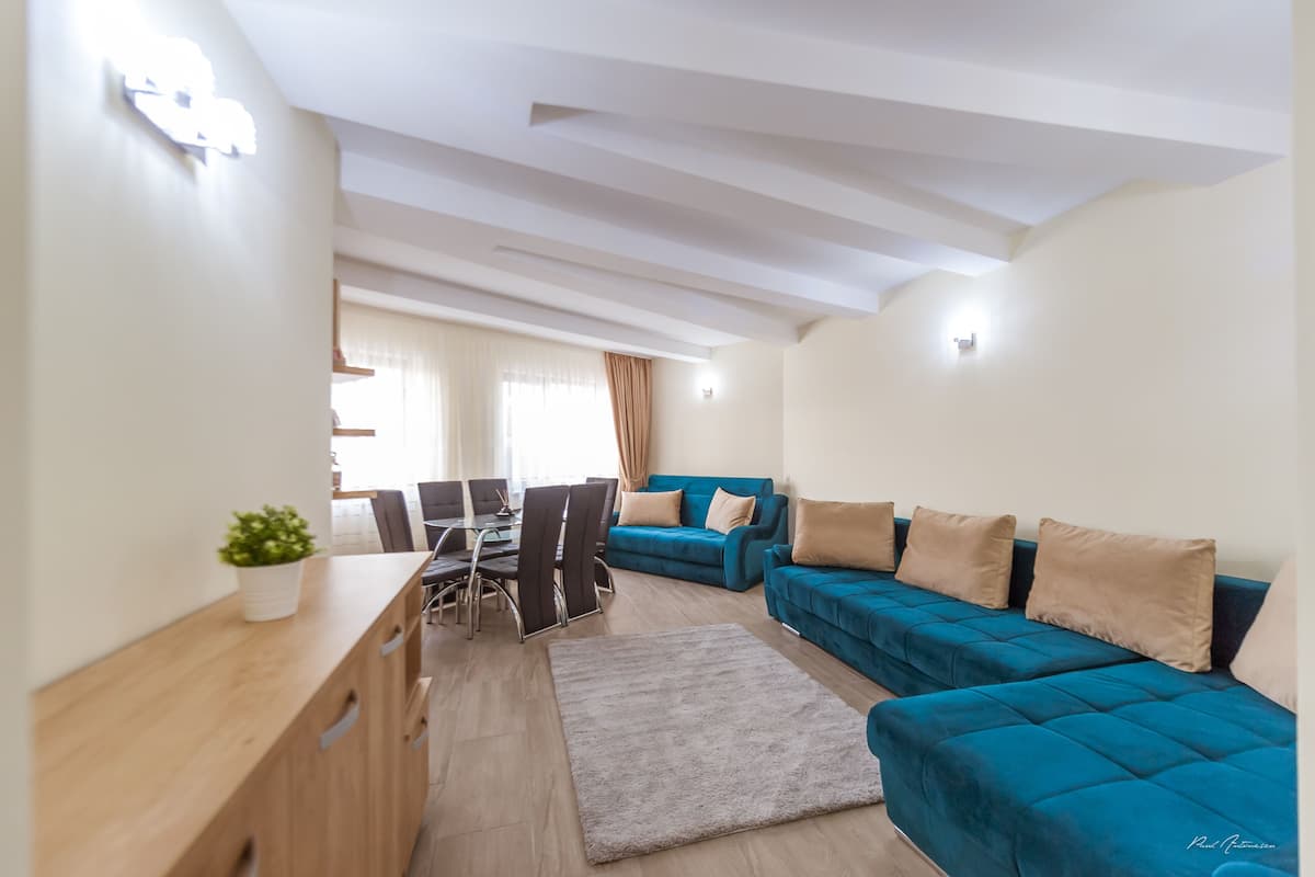 A modern living room with a blue sofa set, a wooden coffee table, and a dining area with a table and chairs.