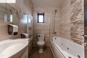 A modern bathroom with a bathtub, toilet, and a small window.