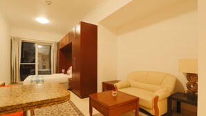 A compact living room with a sofa, a coffee table, a small table, and a window with curtains. - OYO Home 260 Studio Saba 3 Tower (Dubai)