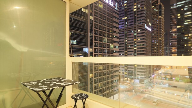 A balcony with a table and a stool, overlooking a cityscape with tall buildings and a busy street. - OYO Home 260 Studio Saba 3 Tower (Dubai)