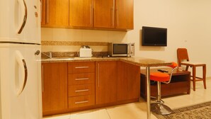 A kitchen with wooden cabinets, a microwave, a toaster, and a TV mounted on the wall. - OYO Home 260 Studio Saba 3 Tower (Dubai)