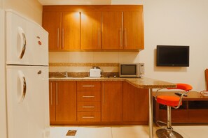 A compact kitchen with wooden cabinets, a white refrigerator, a microwave, and a small TV.