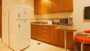 A compact kitchen with a refrigerator, microwave, and a small dining area with a chair. - OYO Home 260 Studio Saba 3 Tower (Dubai)