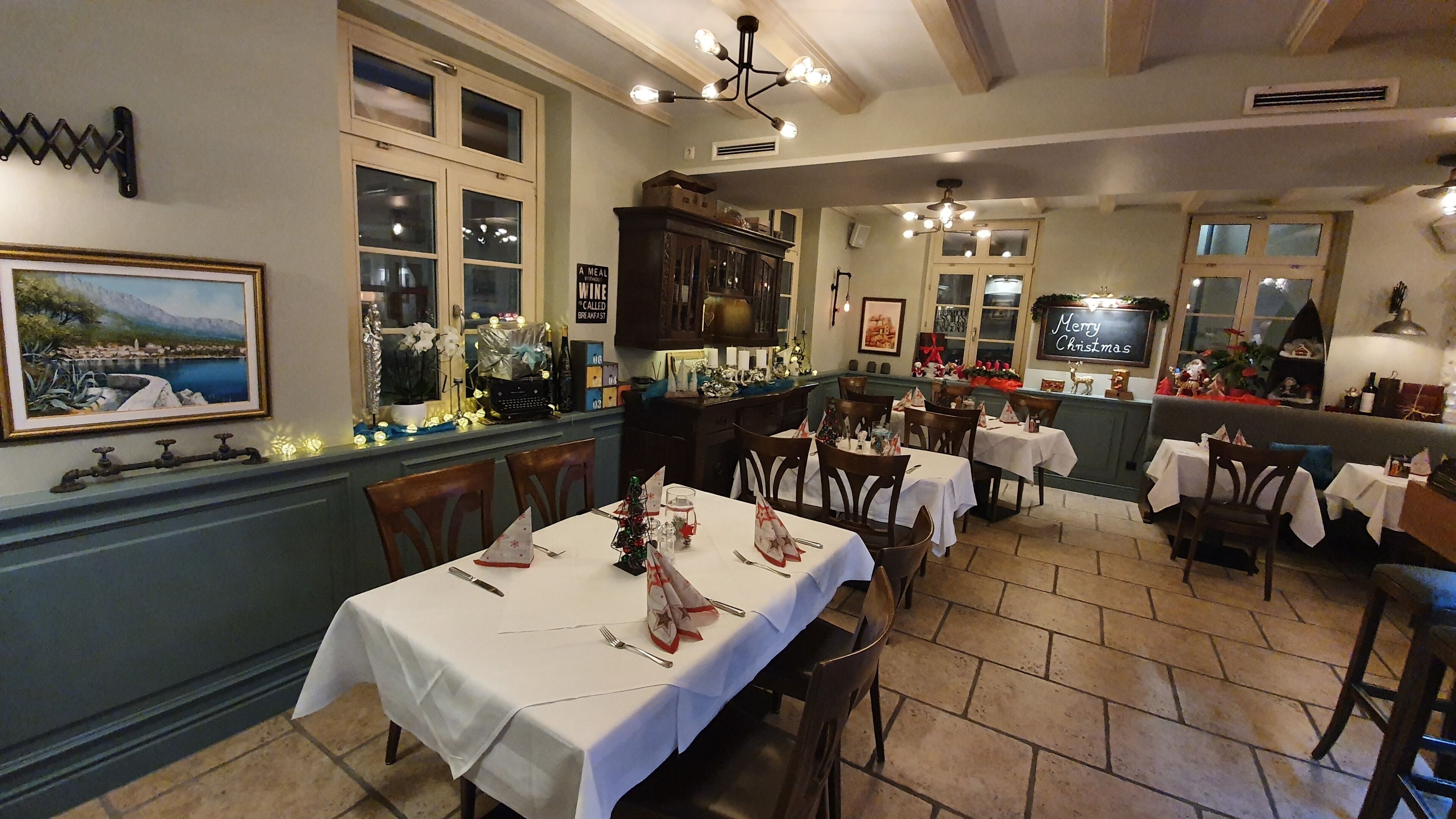 Un restaurante con varias mesas dispuestas para comer, un amplio ventanal con vistas y un cartel que dice 'Merry Christmas'.