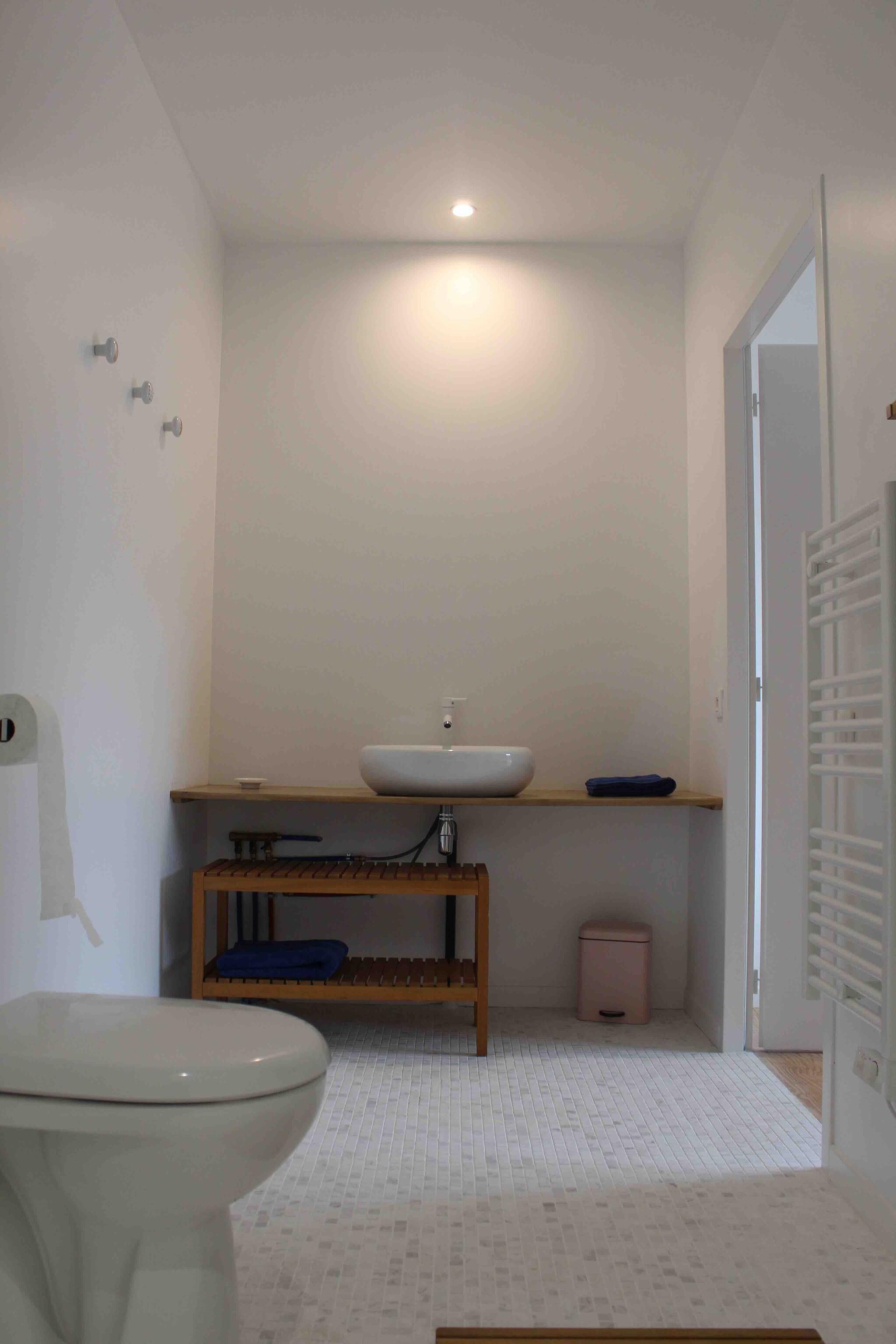 A modern bathroom with a white toilet, a wooden vanity with a sink, and a small trash bin.