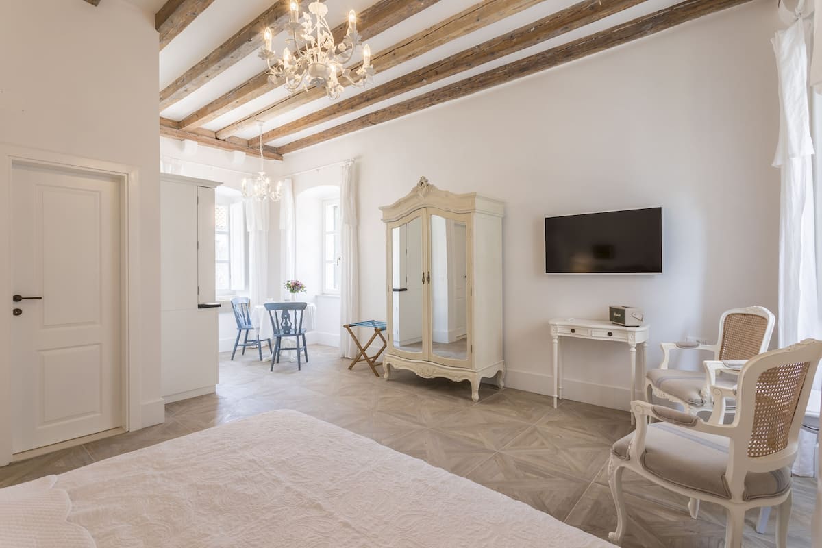 Quarto com uma cama grande, televisão, guarda-roupa e secretária com cadeiras.