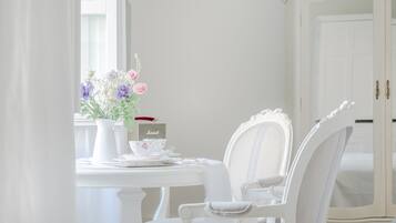 A white dining table with a vase of flowers, a teapot, and cups. A white chair is positioned at the table.