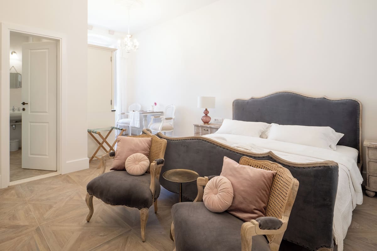 Quarto com uma cama grande, duas poltronas, uma mesinha e um candelabro.