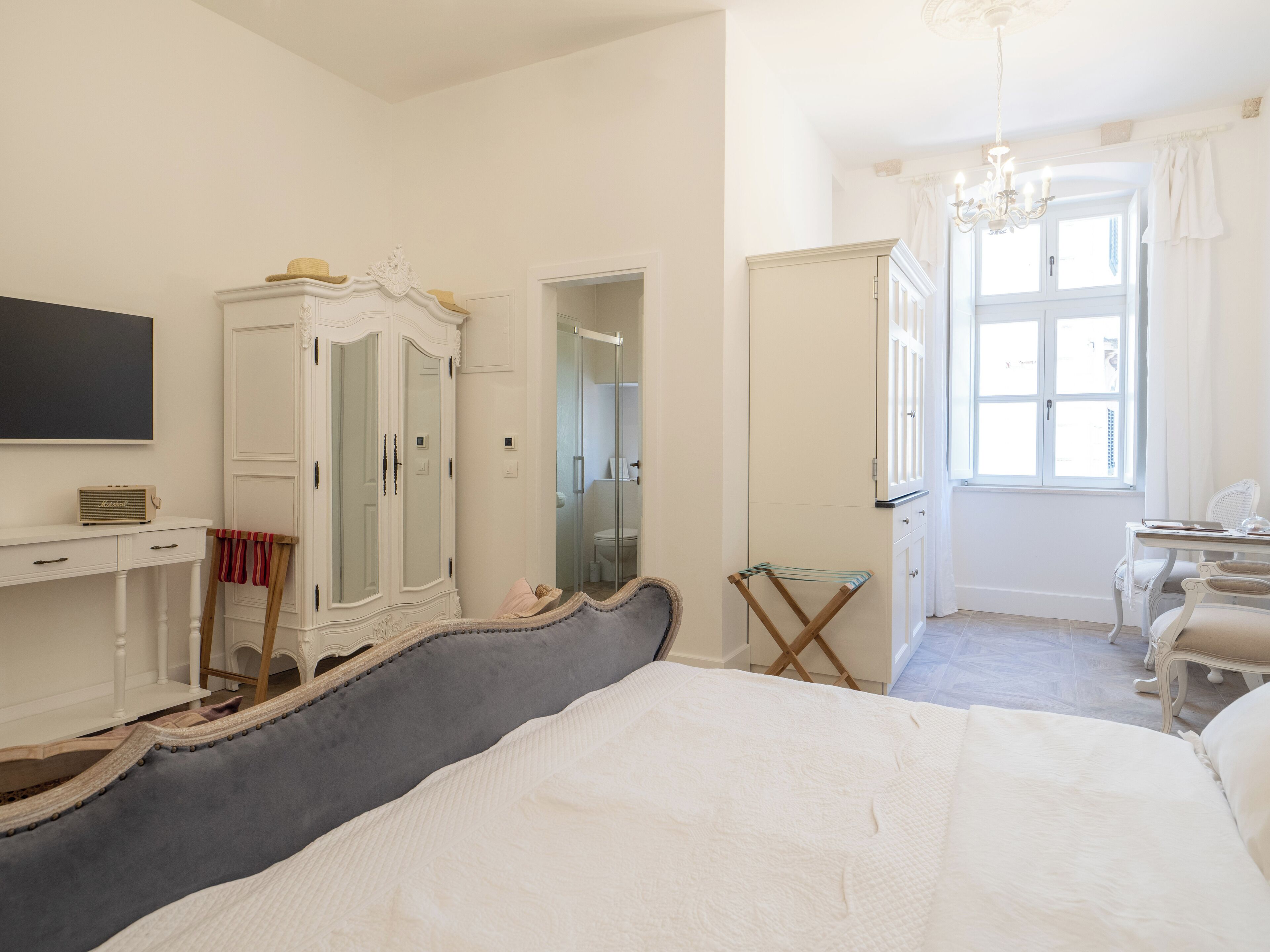 A bedroom with a large bed, a wardrobe, a desk, and a chair.