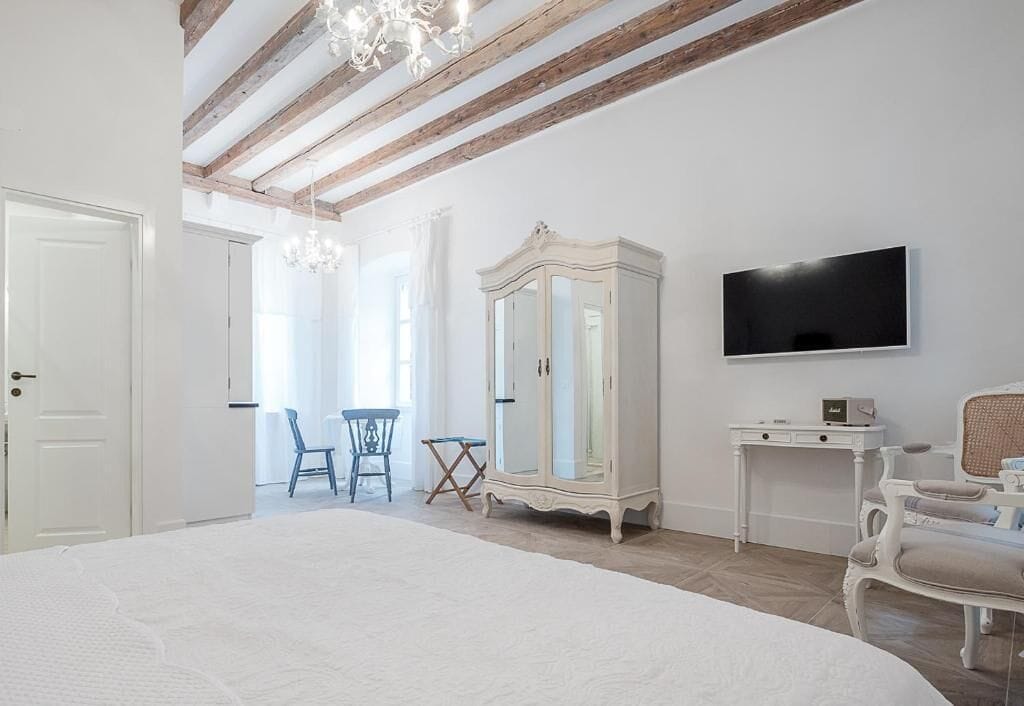 Un dormitorio con una cama grande, un armario, televisión y un rincón comedor con sillas.