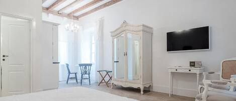 Un dormitorio con una cama grande, un armario, televisión y un rincón comedor con sillas.