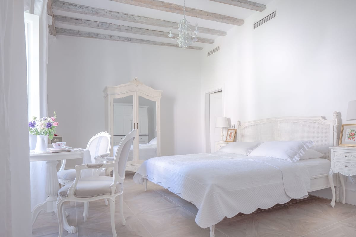 Quarto com cama, cadeira, guarda-roupa e escrivaninha com um vaso de flores.