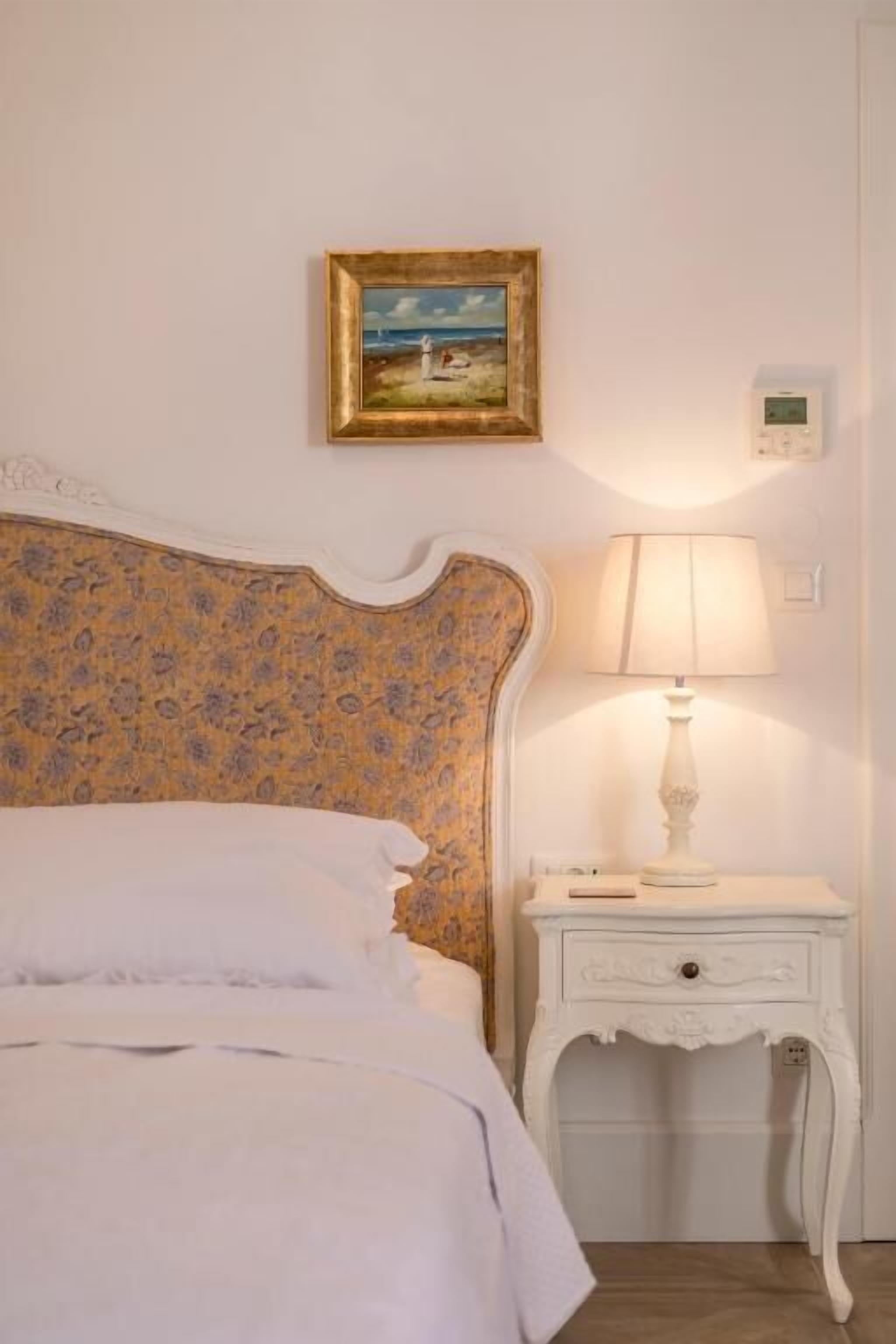 Un dormitorio con un cabecero estampado con motivos florales, una mesita de noche con lámpara y un cuadro enmarcado en la pared.