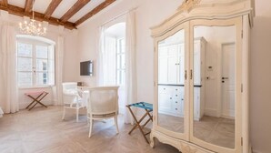 Een kamer met een houten plafond, een grote spiegel, een witte garderobe, een witte stoel en een kleine tafel.