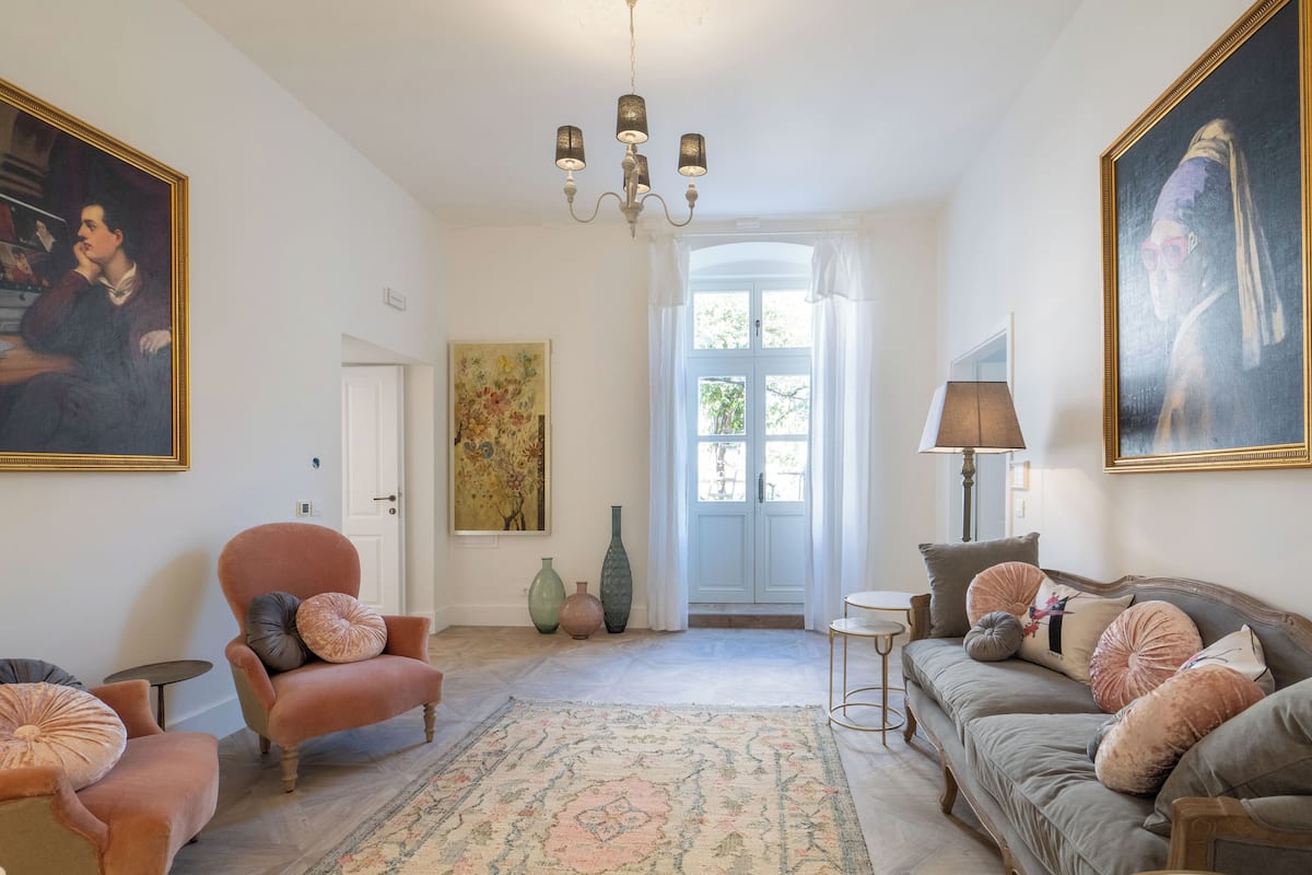 Uma sala de estar com um candelabro, um sofá, uma poltrona e um tapete.