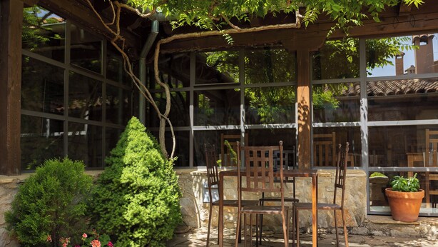 Un patio con mesa y sillas de madera, rodeado de muros de piedra y macetas con plantas.
