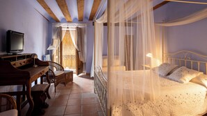 Un dormitorio con cama con dosel, un televisor sobre un escritorio de madera y una silla de mimbre.