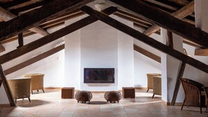 Habitación en ático con vigas de madera a la vista, televisor de pantalla plana montado en la pared y mobiliario de mimbre.
