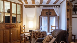 Una habitación acogedora con un armario de madera, un sillón cómodo, una mesa con un libro y una ventana con cortinas.