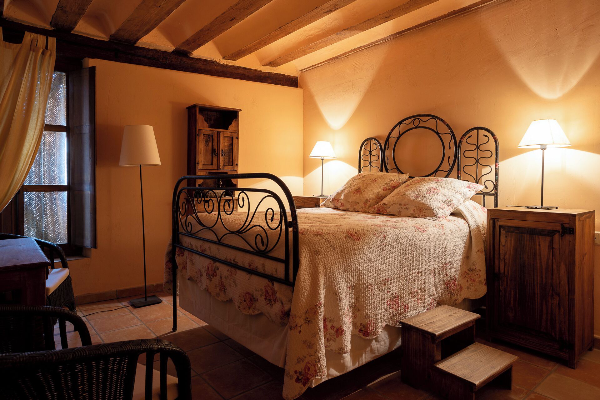 Une chambre confortable avec un lit en bois, deux lampes de chevet, une petite commode en bois et une chaise.