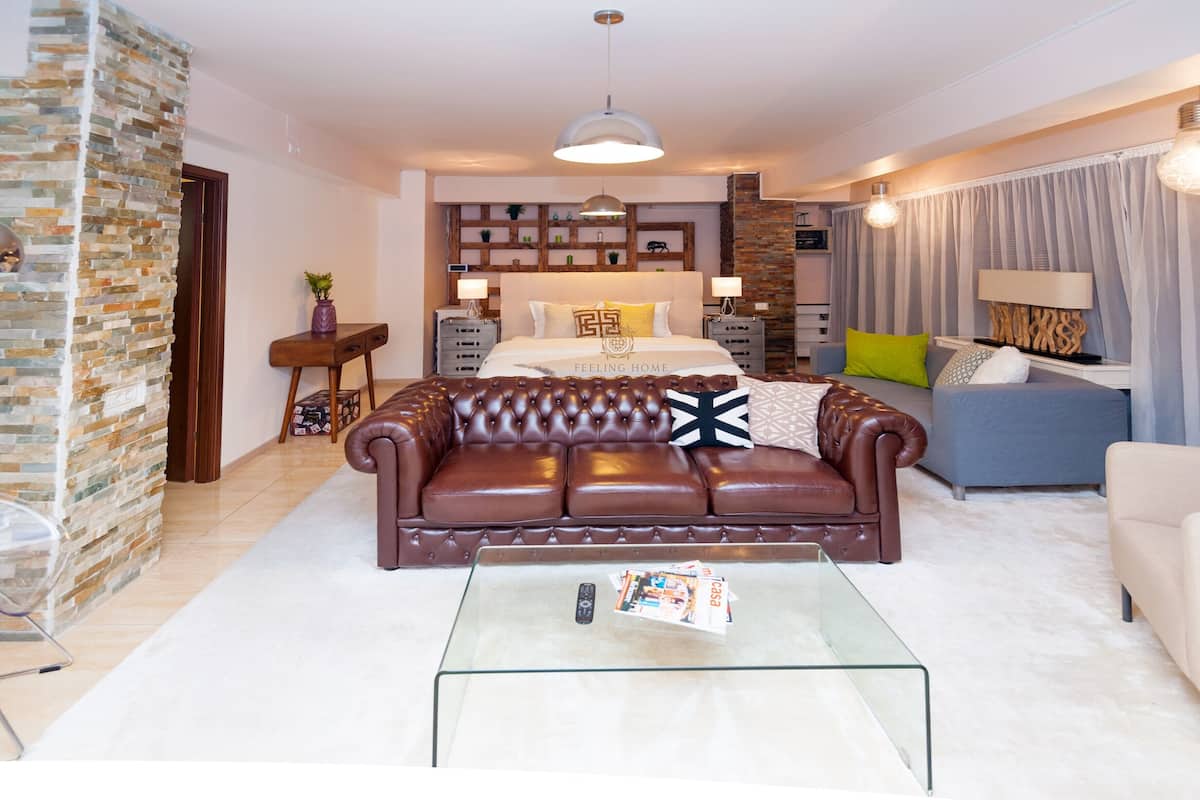 Ein modernes Wohnzimmer mit Ledersofa, Glastisch und einem Bett mit Kopfteil.